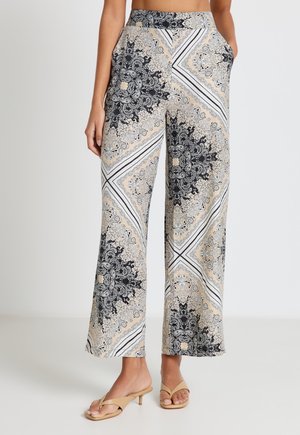 Wide-leg pants with beige and black intricate paisley and geometric pattern, worn with beige heeled sandals.
