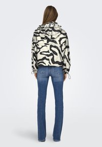 Giacca cropped con cappuccio in un motivo astratto bianco e nero. Presenta polsini elasticizzati, una tasca sul retro e una texture leggermente lucida.