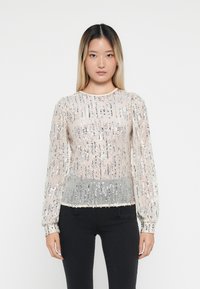 Doorzichtig langemouwen top met een zilveren paillettenpatroon, lichtbeige basis en een geplooide zilveren zoom; ronde halslijn en gathered manchetten.