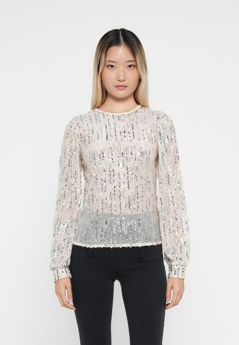 Doorzichtig langemouwen top met een zilveren paillettenpatroon, lichtbeige basis en een geplooide zilveren zoom; ronde halslijn en gathered manchetten.