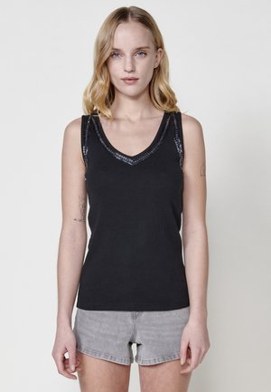 Top nero senza maniche con scollatura a V, caratterizzato da dettagli decorativi in paillettes sulle spalle e una trama a coste aderente.