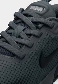 Κοντινή λήψη αθλητικού παπουτσιού σε σκούρο γκρι με υφή πλέγματος, χοντρά κορδόνια και μαύρο σήμα Nike στην πλευρά.