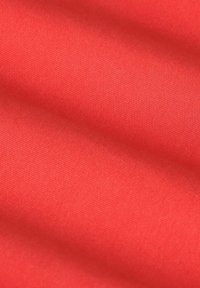 Tissu rouge avec une texture lisse, présentant un motif uniforme et légèrement nervuré, d'une teinte globale vibrante. Pas d'accents distinctifs présents.