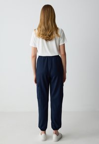 Marineblauwe cargobroek met elastische tailleband en boorden, met twee zijzakken. Gecombineerd met een eenvoudig wit t-shirt.