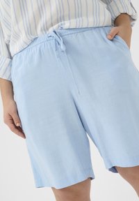 Ljusblå shorts i mjukt tyg med elastisk midja och snörning. Har sidofickor och en avslappnad passform.