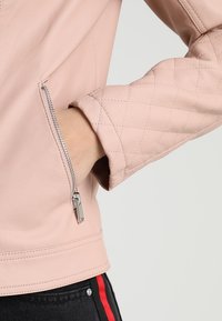 Giacca di pelle rosa chiaro con dettagli imbottiti sulle maniche, zip argentata ai polsi, texture liscia e design aderente.
