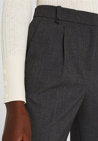 Pantalons taillés gris foncé en tissutexturé, dotés de plis avant et d'une ceinture élégante avec un petit accent en métal.