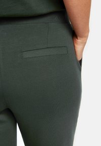 Pantalon vert foncé avec une texture de tissu lisse, doté d'une seule poche arrière avec une finition de couture propre.