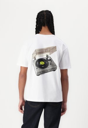 White T-shirt featuring a graphic of a vintage turntable with a vinyl record, text "the new originals" in black along the bottom. Casual fit.
