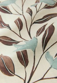 Stoff mit floralem Design, das blaue Blätter und braune Stängel auf einem cremefarbenen Hintergrund zeigt und eine strukturierte Optik erzeugt.