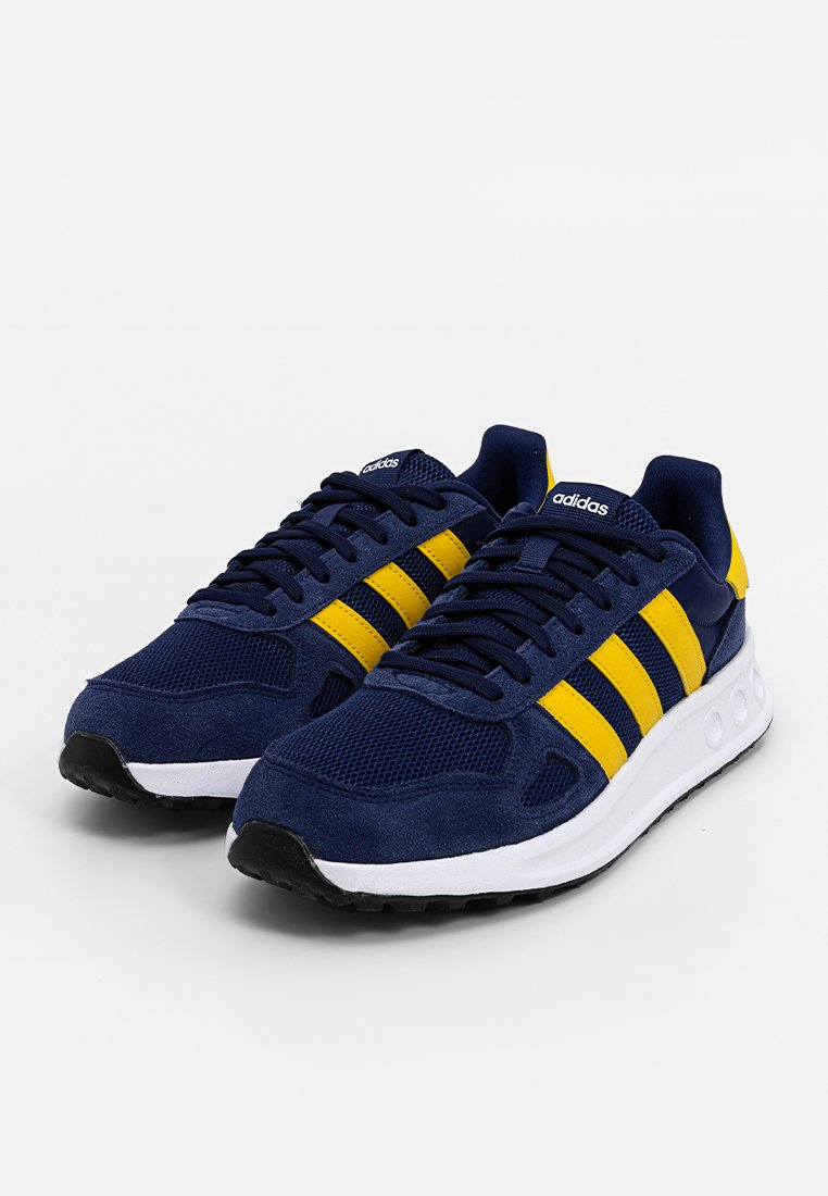 Granatowe buty sportowe z żółtymi paskami, wykonane z siateczki i zamszu, z białą podeszwą środkową i czarną gumową podeszwą.