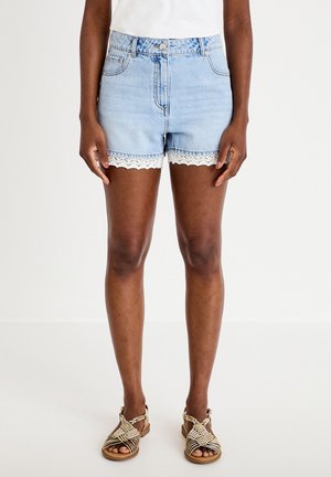 Mid-length light blue denim shorts with white lace trim worn by a person standing, paired with light woven flat sandals.