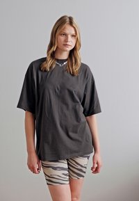 Černé oversized tričko vyrobené z bavlny, spárované s béžovými šortkami s vzorem zebřích pruhů. Hladká textura a uvolněný střih.