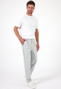 Grijze geplooide broeken met een relaxed fit, gecombineerd met een wit T-shirt met korte mouwen. Witte sneakers maken de look compleet.