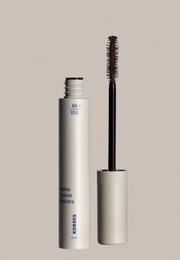 Valkoinen sylinterimäinen ripsiväriputki, jossa on sinistä tekstiä. Musta varsi, jossa on pyöreät harjakset. Kannen pinta on uritettu.