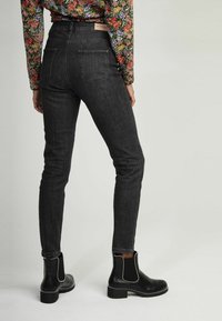 Černé skinny džíny s vysokým pasem, zadními kapsami a jemnou texturou, doplněné černými kotníkovými botami se stříbrnými detaily.