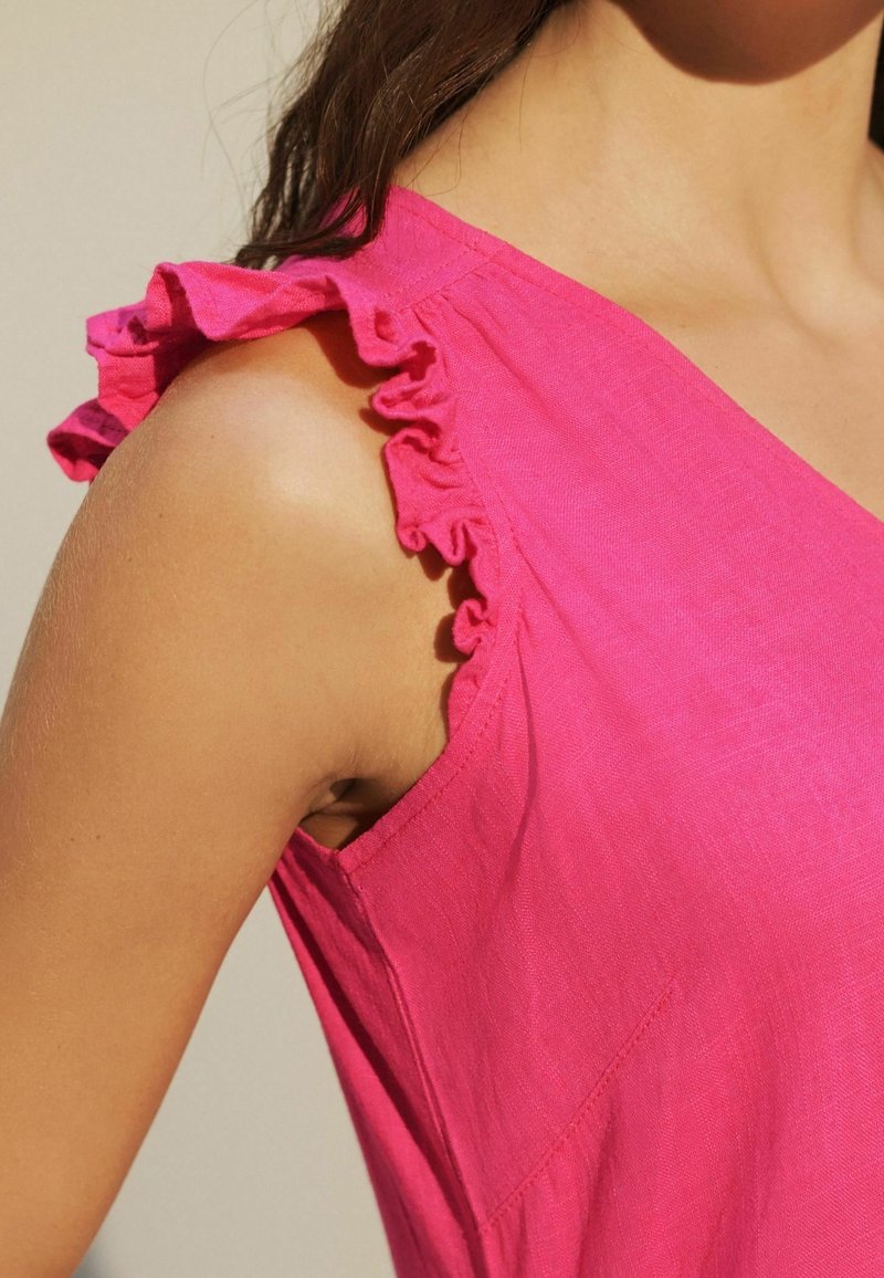 Top de lino fucsia con acentos de hombros con volantes y un diseño de escote en V. Textura suave con un discreto detalle de bolsillo lateral.