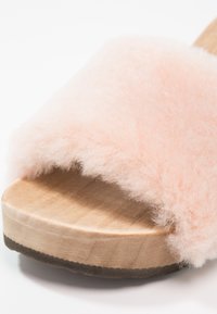 Růžové nadýchané skluzové sandály s měkkým, huňatým svrškem a přírodním dřevěným podešví, mají zaoblenou špičku a hladkou texturu.