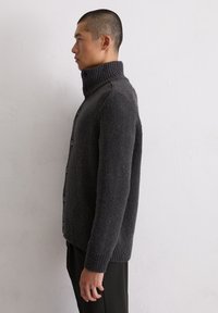 Cardigan en maille gris foncé avec un col haut, une fermeture à boutons à l'avant et des poignets côtelés. Il présente un tissu texturé et une silhouette ajustée.