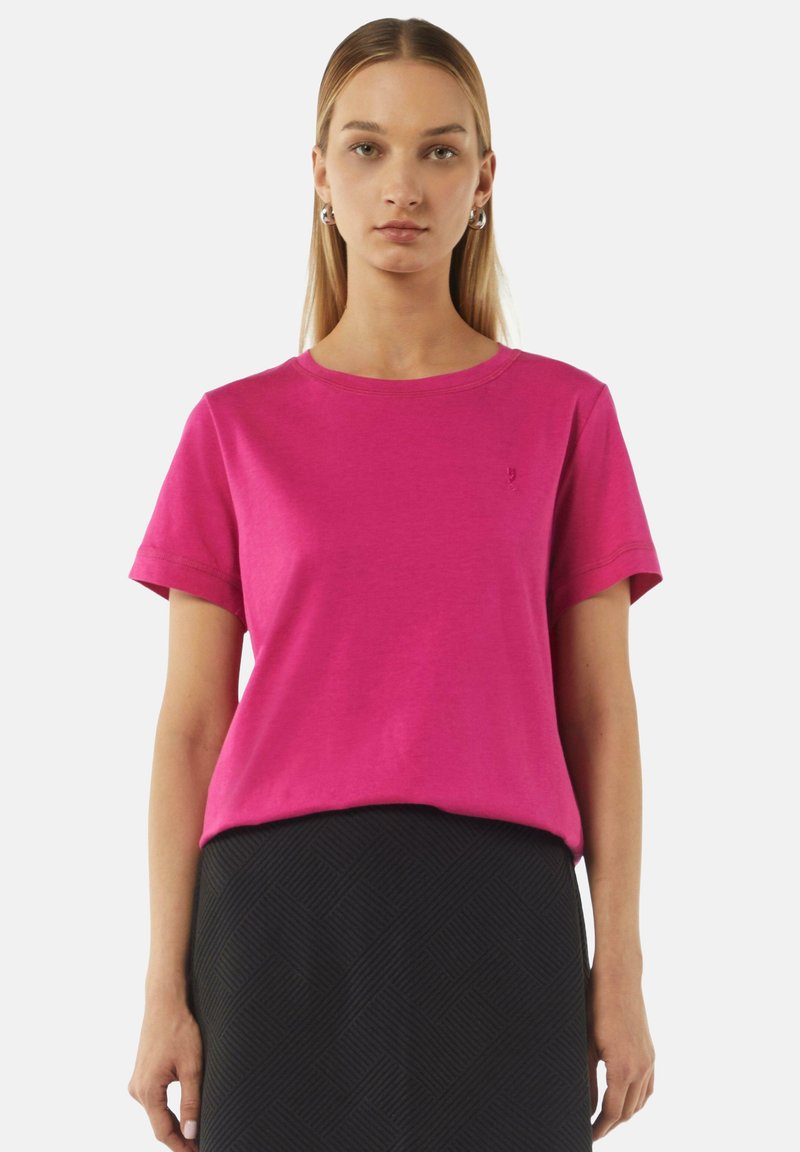 Fuchsia Baumwoll-T-Shirt mit kurzen Ärmeln, Rundhalsausschnitt und dezentem Logodetail. Kombiniert mit einem strukturierten schwarzen Rock.