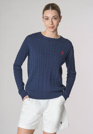 Pullover navy a maglia cable con scollatura rotonda e polsini a coste. Abbinato a pantaloni corti bianchi con un piccolo logo ricamato sull'orlo.
