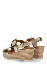 Sandalias de cuña en beige con una correa texturizada dorada y un gran hebilla dorada. La suela elevada tejida en yute añade textura y altura.