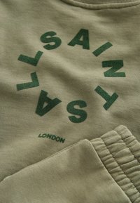 Olivgrüner Baumwoll-Sweatshirt mit einem kreisförmigen grünen Grafik, auf der das Wort "SAINTS" und "LONDON" am unteren Rand steht, strukturierter Druck und gerippte Bündchen.