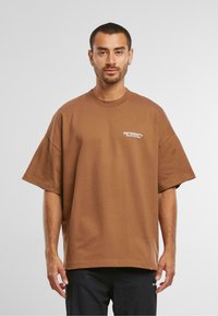 Brun oversized t-shirt lavet af bomuld, med korte ærmer og rund halsudskæring. Fronten viser hvid tekst.