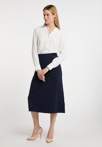 Bílá košile s dlouhými rukávy, spárovaná s přiléhavou námořnickou tužkovou sukni a holými lodičkami na vysokém podpatku. Minimalistický design a čisté linie.