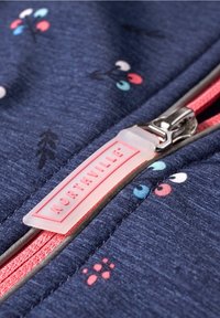 Gros plan sur une fermeture éclair en tissu bleu avec des dents roses, une tirette translucide portant l'inscription "NORTHVILLE", et de petits motifs floraux colorés imprimés.