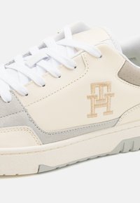 Sneaker bianchi e grigi con textures in pelle e camoscio, dotati di lacci bianchi, una suola morbida e un logo ricamato in beige.
