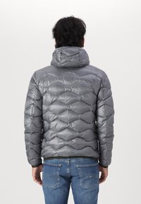 Graue Puffjacke mit einem gesteppten Design, ausgestattet mit einer Kapuze und glänzender Optik. Kombiniert mit blauen Jeans, die eine lässige Rückenansicht zeigen.