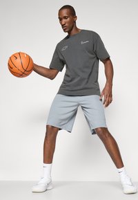 Gray cotton t-shirt with white logos and light blue shorts. White sneakers with textured soles. Holding an orange basketball.