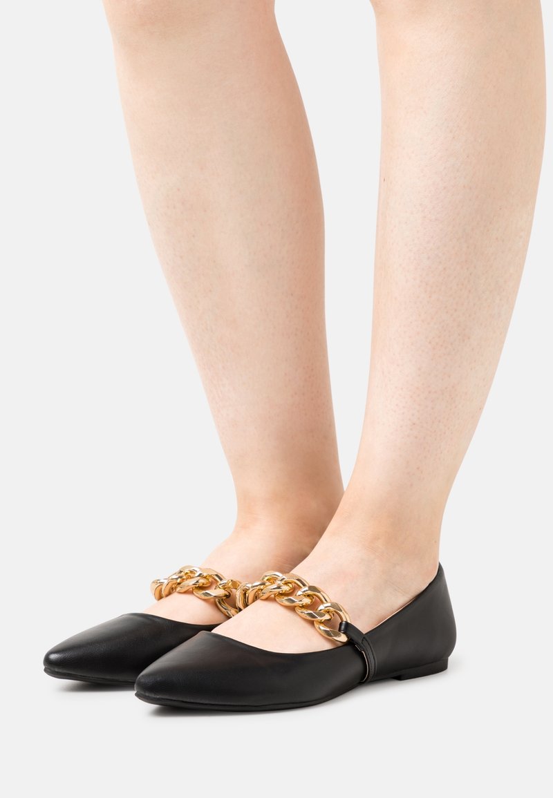 Bailarinas de piel negra con punta afilada, adornadas con una cadena dorada en la parte superior. Diseño de perfil bajo con un tacón redondeado.
