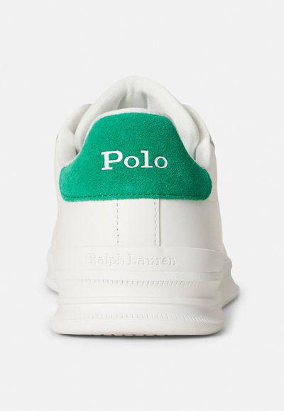 Biała skórzana sportowa tenisówka z zielonym zamszowym wzmocnieniem na pięcie. Na boku wytłoczone napisy "Polo" i "Ralph Lauren" w białym kolorze. Gładka tekstura i smukły, nowoczesny design.