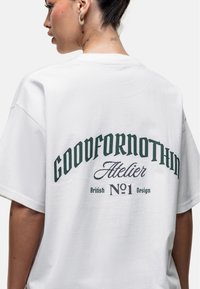 Biała, oversize'owa koszulka wykonana z bawełny, z zielonym napisem "GOODFORNOTHING Atelier British No.1 Design" z tyłu.