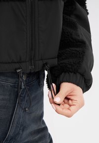 Giacca nera con un design in pile morbido e testurizzato. Presenta polsini elasticizzati e regolazioni con coulisse all'orlo per una vestibilità personalizzabile.