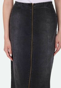 Sort denimnederdel med en central lynlås i guldhardware, med sidesømme og lige silhuet. Glat tekstur og knælængde design.