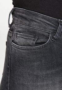 Jeans negros de mezclilla con un corte ajustado. Cuentan con un bolsillo trasero, costuras resistentes y una cinturilla de altura media. Textura suave.