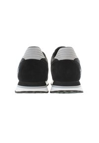 Svarta träningsskor med överdel i mocka och mesh, med grå ribbade detaljer, vit mellansula och strukturerad svart yttersula.