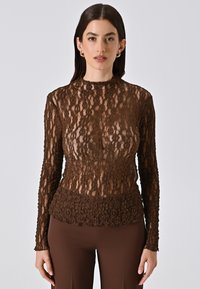 Top in pizzo marrone con maniche lunghe e colletto alto, caratterizzato da un motivo floreale testurizzato. Tessuto trasparente con una silhouette aderente.