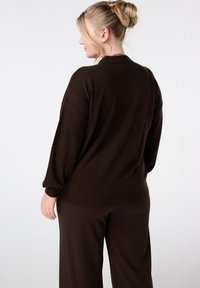 Bruine oversized trui met geribbelde manchetten en boord, voorzien van een zachte textuur en een ontspannen pasvorm, gecombineerd met bijpassende donkerbruine broek.