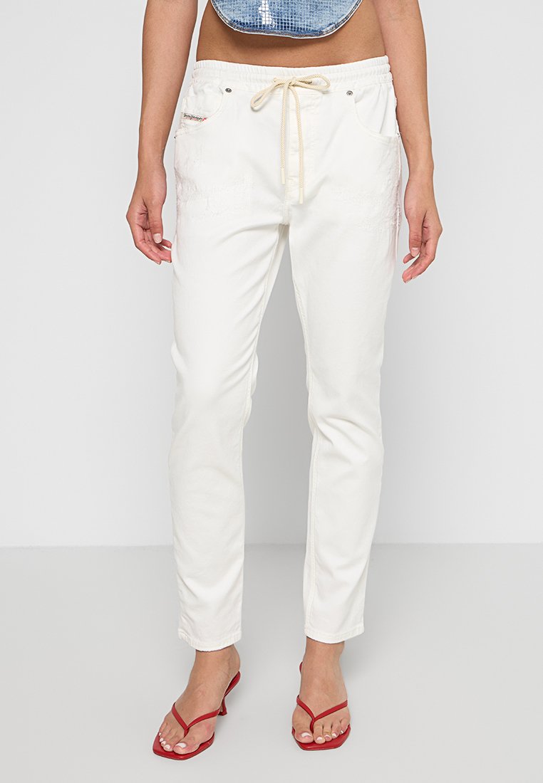 Weiße, lässig geschnittene Hose mit Zugbund, zwei Seitentaschen und dekorativen Nähdetails. Kombiniert mit roten Sandalen.