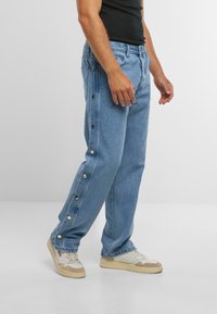Hellblaue Jeans aus Denim verfügen über seitliche Druckknöpfe, einen lässigen Schnitt und ein gerades Bein-Design. Kombiniert mit weißen und beige Sneakers.