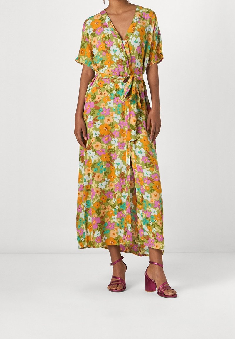 Blomstret omslagskjole i gul, grøn og pink med korte ærmer og en bånddetalje i taljen. Matchet med pink hælesandaler.