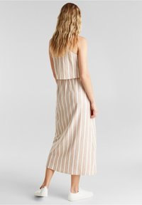 Olkaimeton, kaksiosainen mekko, jossa pystysuorat beiget ja ruskeat raidat, lyhyt yläosa ja liehuva midihelmainen hame; yhdistetty valkoisiin tennareihin.