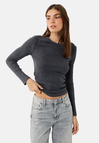 Donkergrijze longsleeve geribbelde top met een ronde halslijn, een getailleerde vorm en subtiele textuur, gecombineerd met lichtgewassen rechte jeans.