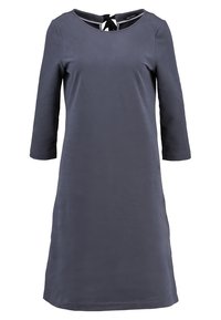 Tummansininen, polvipituinen mekko, jossa on kolmantena osana hihat, pyöreä pääntie ja takataskusi yksityiskohtana. Valmistettu sileästä kankaasta, jossa on minimaalinen tekstuuri.