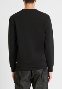 Sudadera negra con cuello redondo, mangas largas y puños de canalé. Fabricada en suave material de forro polar con dobladillo recto. Sin patrones visibles.
