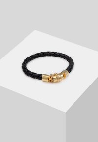 Bracciale in pelle intrecciata nera con chiusura in metallo tono oro e un accento decorativo. Texture liscia e costruzione robusta.